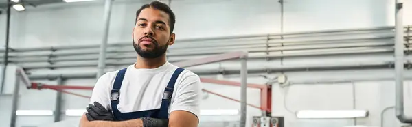A handsome young mechanic stands proudly with arms crossed in an industrial workshop setting. — Stock Photo