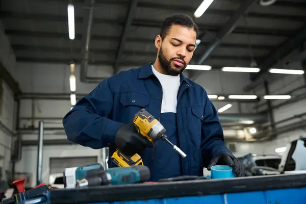 Handsome young mechanic uses a power drill while focusing on a task in a busy workshop. — Stock Photo