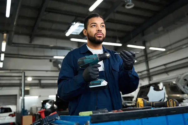Handsome young mechanic focuses on his task amidst a busy auto repair workshop environment. — Stock Photo