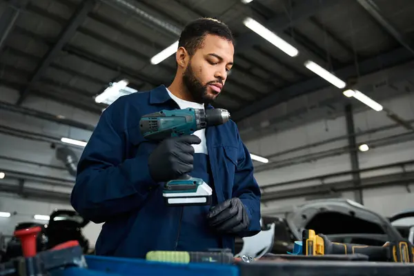 Un joven mecánico experto se centra en el uso de una herramienta eléctrica en un taller de reparación de automóviles ocupado. - foto de stock