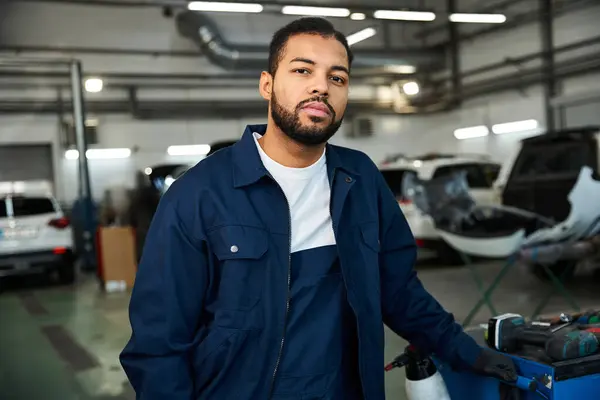 Handsome young mechanic stands confidently while working in a bright and busy garage area — Stock Photo