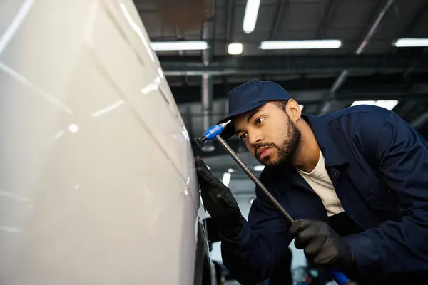 Jeune mécanicien inspecte soigneusement un véhicule au milieu des outils dans l'atelier. — Photo de stock