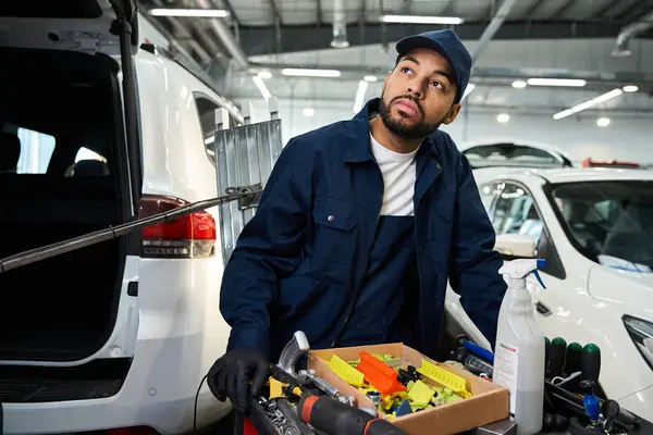 Handsome mechanic examines tools while standing beside a vehicle in a modern workshop. — Stock Photo
