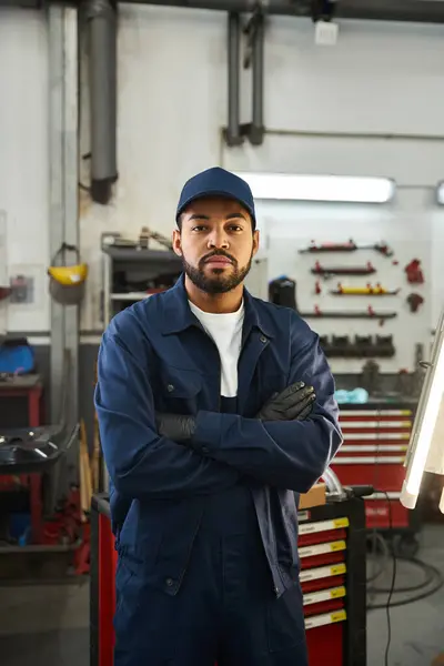 A skilled young mechanic stands proudly in a lively garage, showcasing his expertise and passion. — Stock Photo