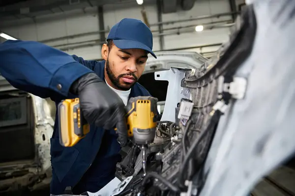 Handsome young mechanic focuses intently while repairing a vehicle in his workplace. — Stock Photo
