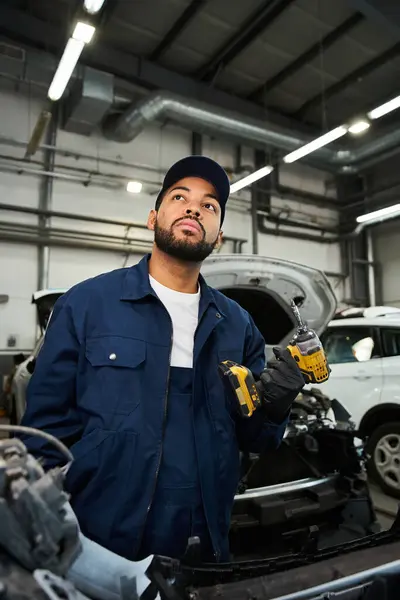 Um jovem mecânico com uma expressão pensativa segura ferramentas enquanto trabalha em uma garagem movimentada. — Fotografia de Stock