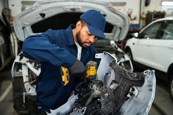 A handsome young mechanic focuses on fixing a vehicle in a busy automotive garage. — Stock Photo