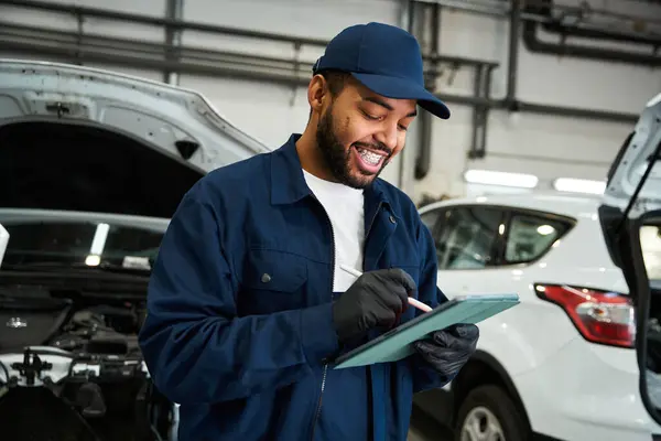 Le mécanicien vérifie les détails du véhicule tout en souriant dans un garage bien équipé pendant les heures de grande affluence — Photo de stock