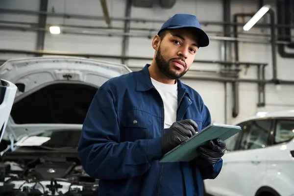 Skilled mechanic in uniform reviews notes with focus in a well lit automotive workshop setting — Stock Photo