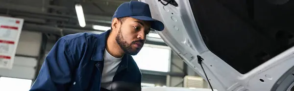 Handsome mechanic intently examining the engine of a vehicle in a well lit garage space. — Stock Photo