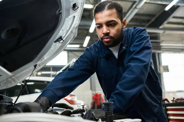 A skilled mechanic focuses intently while repairing an engine in a bright garage. — Stock Photo