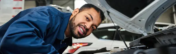 A young mechanic smiles while inspecting an engine under the hood in a vibrant workshop — Stock Photo