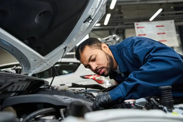 Handsome mechanic repairs a car engine while focusing intently in a busy workshop space. — Stock Photo