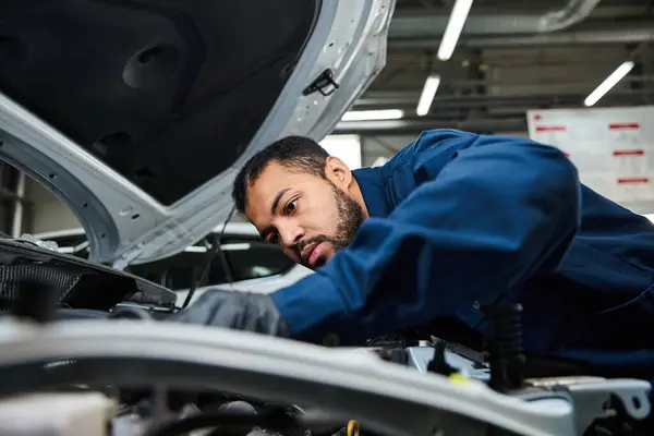 A skilled young mechanic focuses on fixing a vehicle under the hood in a bustling workshop. — Stock Photo