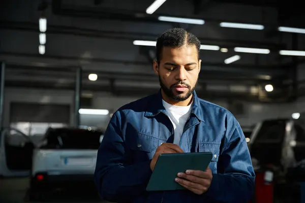 Young mechanic examines data on a tablet while surrounded by vehicles in a well lit workshop — Stock Photo