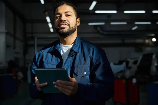 Handsome mechanic stands confidently with tablet in hand, focused on his work in the garage. — Stock Photo