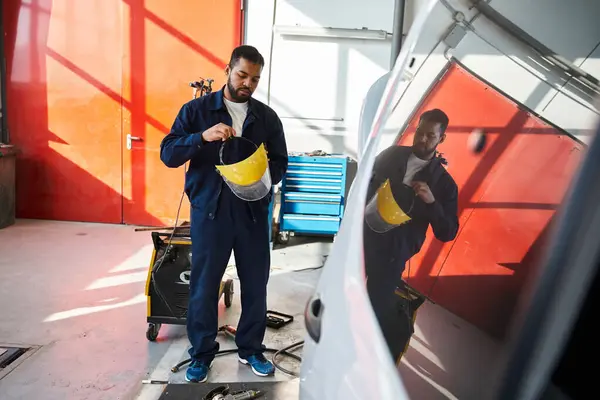 Young and handsome mechanic adjusts his protective gear in a modern garage setting — Stock Photo