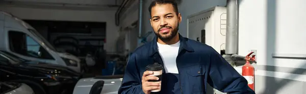 Bello giovane meccanico si prende un momento per rilassarsi con un caffè mentre circondato da veicoli. — Foto stock