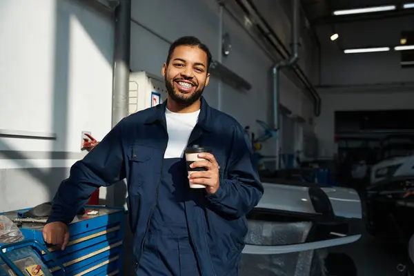 Confident young mechanic sips coffee, surrounded by tools and equipment. — Stock Photo