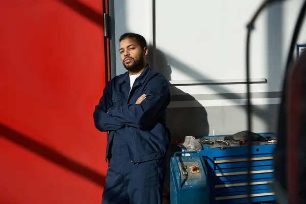 Handsome young mechanic leans against a wall, enjoying a moment of relaxation at work. — Stock Photo
