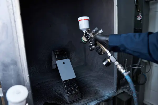 Handsome mechanic focuses intently as he sprays paint inside a working area. — Stock Photo