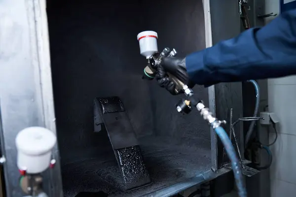 A skilled young mechanic is carefully painting a car part in a clean, well lit workshop. — Stock Photo