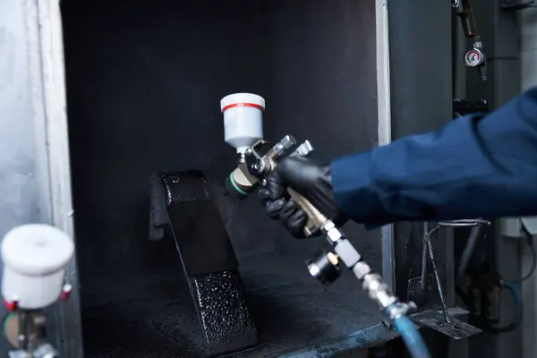 Bonito jovem mecânico se concentra em pintar uma peça de carro em um ambiente de oficina profissional. — Fotografia de Stock