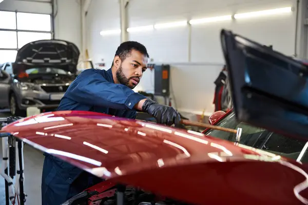 Schöne junge Mechaniker konzentrierte sich auf die Reparatur eines roten Autos in einem hellen Garagenumfeld — Stockfoto