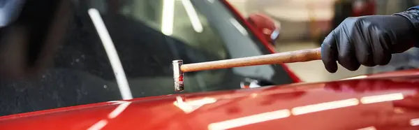 Un mecánico talentoso fijando un exterior rojo de los coches con precisión mientras que la luz del sol vierte adentro. - foto de stock