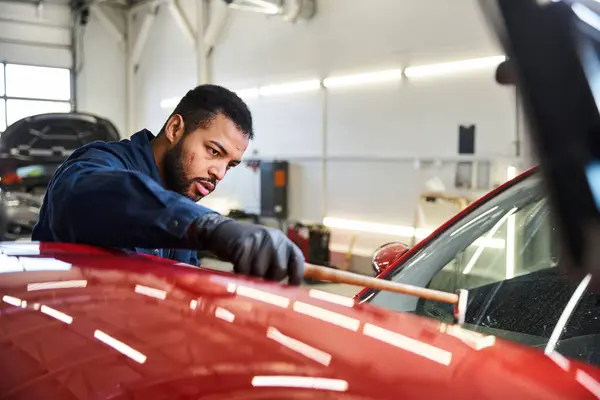 Young man meticulously repairs a red car while focused on his task in a garage setting. — Stock Photo