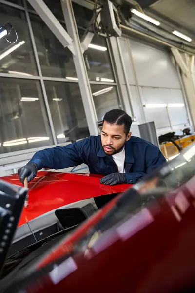 Un jeune mécanicien concentré inspecte la surface d'une voiture dans un atelier lumineux et bien équipé. — Photo de stock