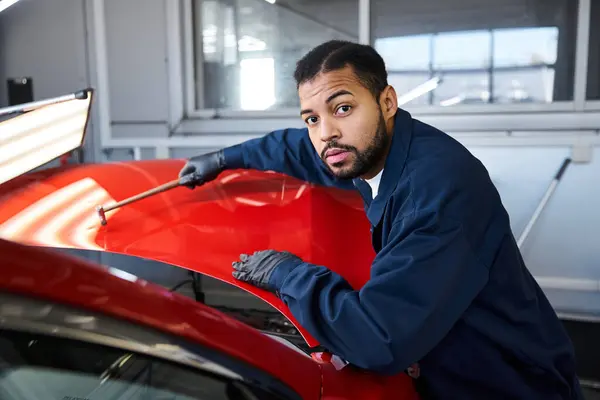 A young mechanic inspects a bright red car under the workshop lights, focused on his work. — Stock Photo