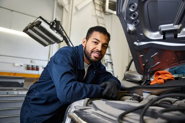 A skilled young mechanic smiles while inspecting an engine under a bright garage light — Stock Photo