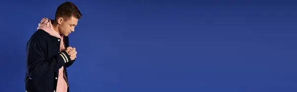 Young man stands in deep thought against a solid blue background. — Stock Photo