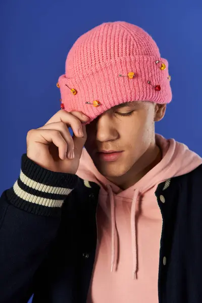 A young man in a pink beanie and hoodie poses, adjusting his hat against a bright backdrop. — Stock Photo