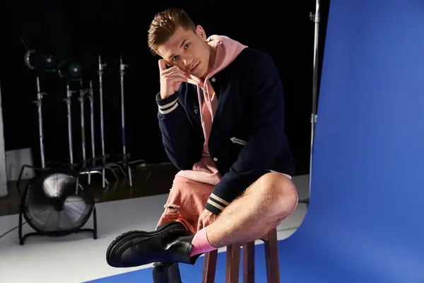 Young man with prosthetic leg sits on a stool wearing fashionable clothes, contemplating. — Stock Photo