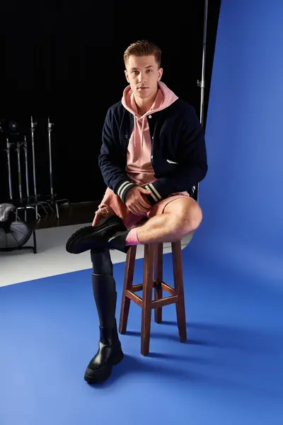 Young man showcases his prosthetic leg while sitting on a stool in a studio environment. — Stock Photo