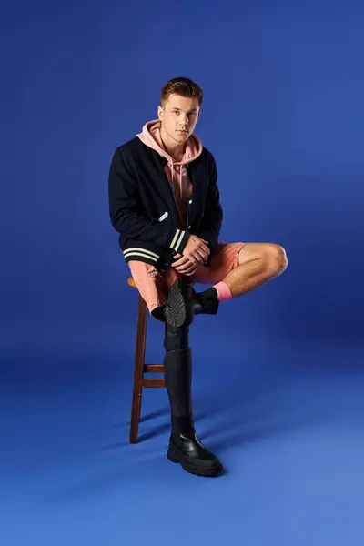 Young man shows off his stylish outfit and prosthetic leg while sitting on a stool. — Stock Photo