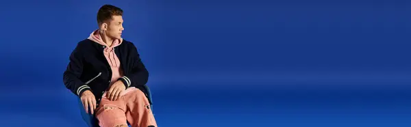 Stylish young man exudes confidence and strength on blue backdrop. — Stock Photo