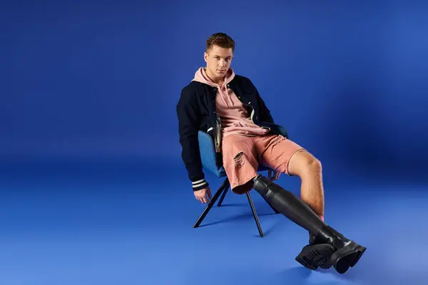 Young man poses confidently while seated, showcasing his stylish attire and prosthetic leg. — Stock Photo