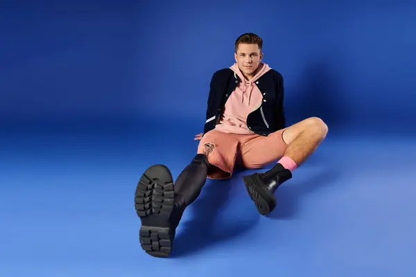 Young man displays his prosthetic leg while seated against a vibrant blue backdrop. — Stock Photo