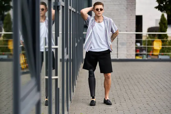 Handsome young man with a prosthetic leg poses confidently near modern glass architecture. — Stock Photo