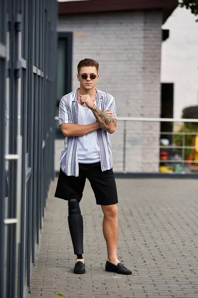 Young man with a prosthetic leg stands confidently, enjoying a sunny urban atmosphere. — Stock Photo