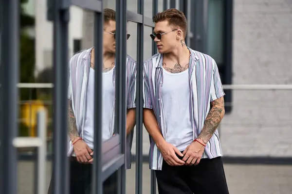 A young man stands by reflective glass, showing his style and confidence. — Stock Photo