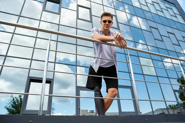 Handsome young man with prosthetic leg enjoys a sunny day near a contemporary structure. — Stock Photo