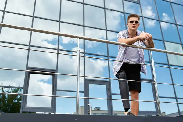 Young man with a prosthetic leg poses confidently in a stylish outfit against a sleek building. — Stock Photo