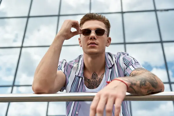 Handsome man adjusts his sunglasses while leaning against a railing. — Stock Photo