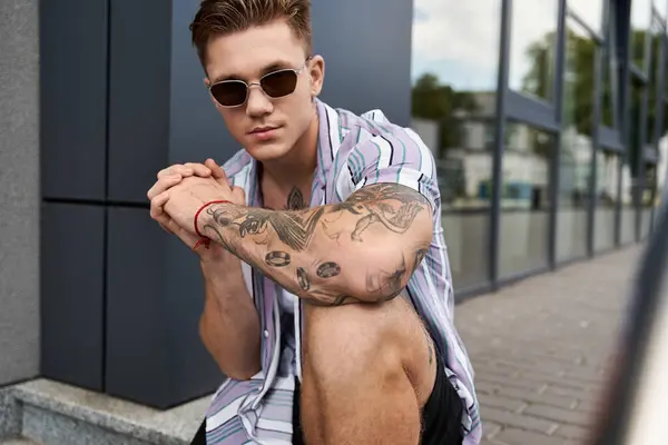 Confident young man with tattoos and sunglasses proudly shows his style in the city. — Stock Photo