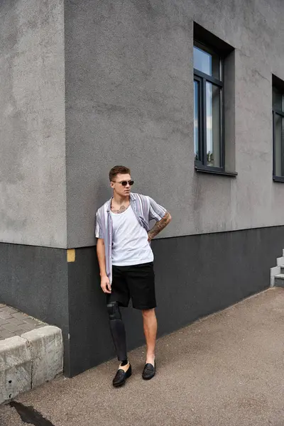 Young man with prosthetic leg stands stylishly against a gray building wall. — Stock Photo