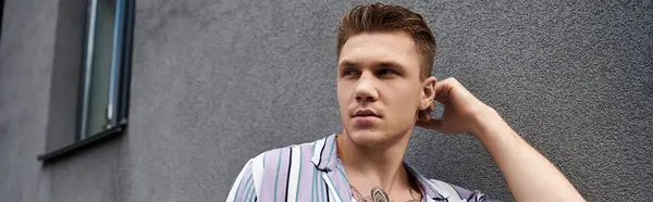 Молодий чоловік з татуюваннями вражає впевнену позу біля текстурованої сірої стіни. — Stock Photo